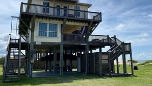 Una casa frente a la playa de dos pisos con un balcón y una escalera, y un letrero que dice "The Love Shack".