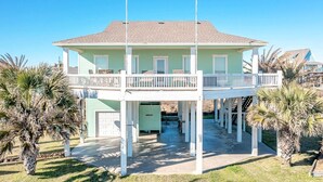 A two-story house with a balcony, surrounded by palm trees. - Parrot Head 3 Bedroom Home by RedAwning (Port Bolivar)