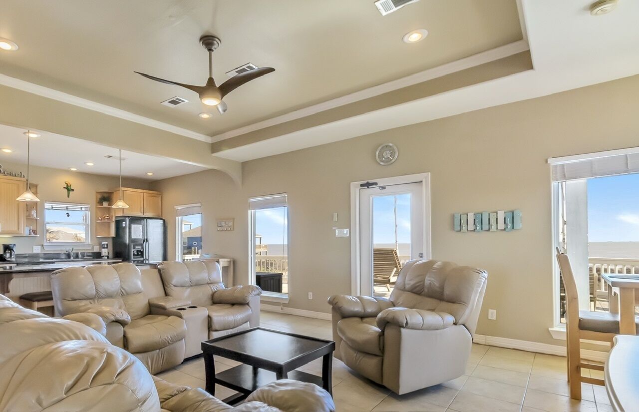 A spacious living area with leather sofas, a coffee table, and a ceiling fan.