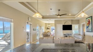 A spacious living area with a large dark marble island, beige sofas, and a ceiling fan. - Parrot Head 3 Bedroom Home by RedAwning (Port Bolivar)