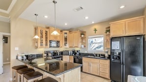A modern kitchen with a large island, wooden cabinets, and a black refrigerator. - Parrot Head 3 Bedroom Home by RedAwning (Port Bolivar)