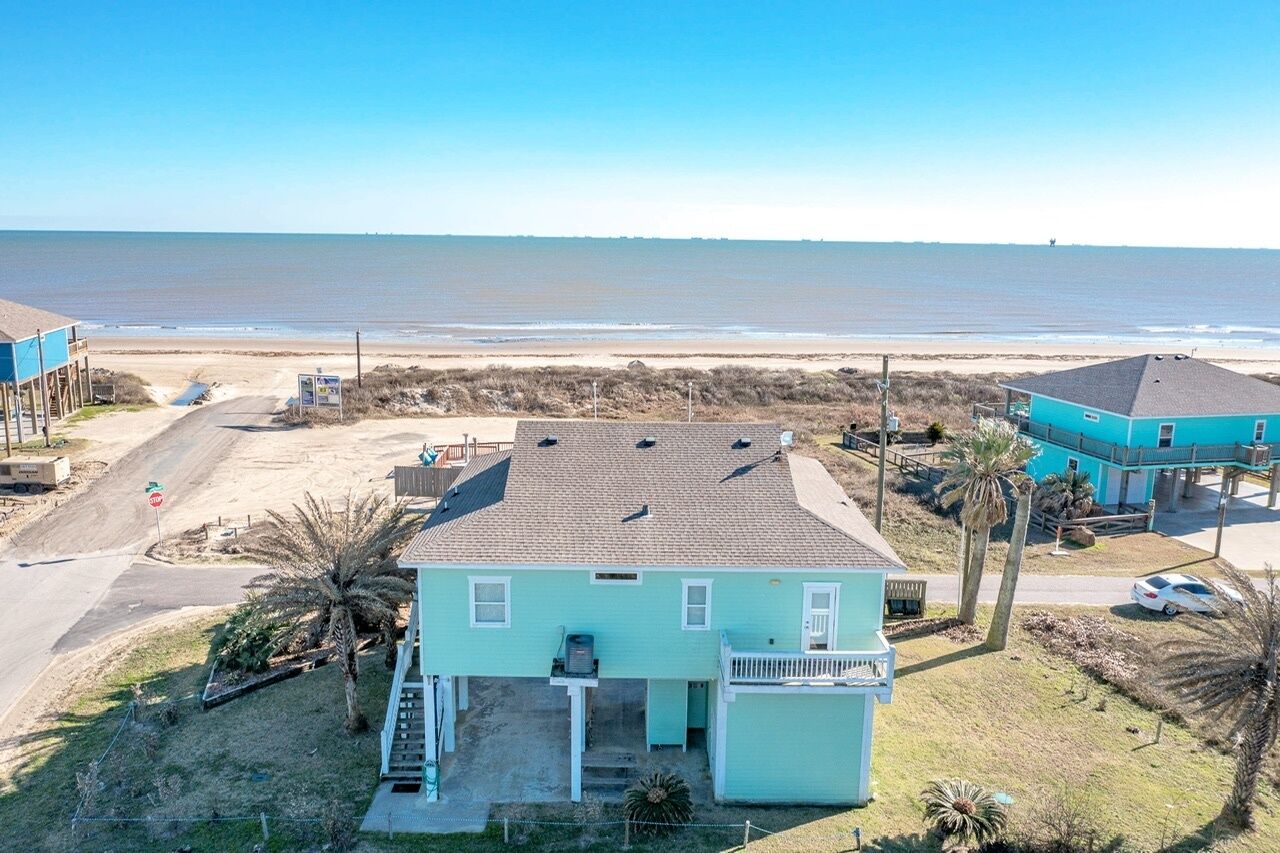 Una casa azul claro con balcón, ubicada cerca de una playa y con vista despejada al océano.