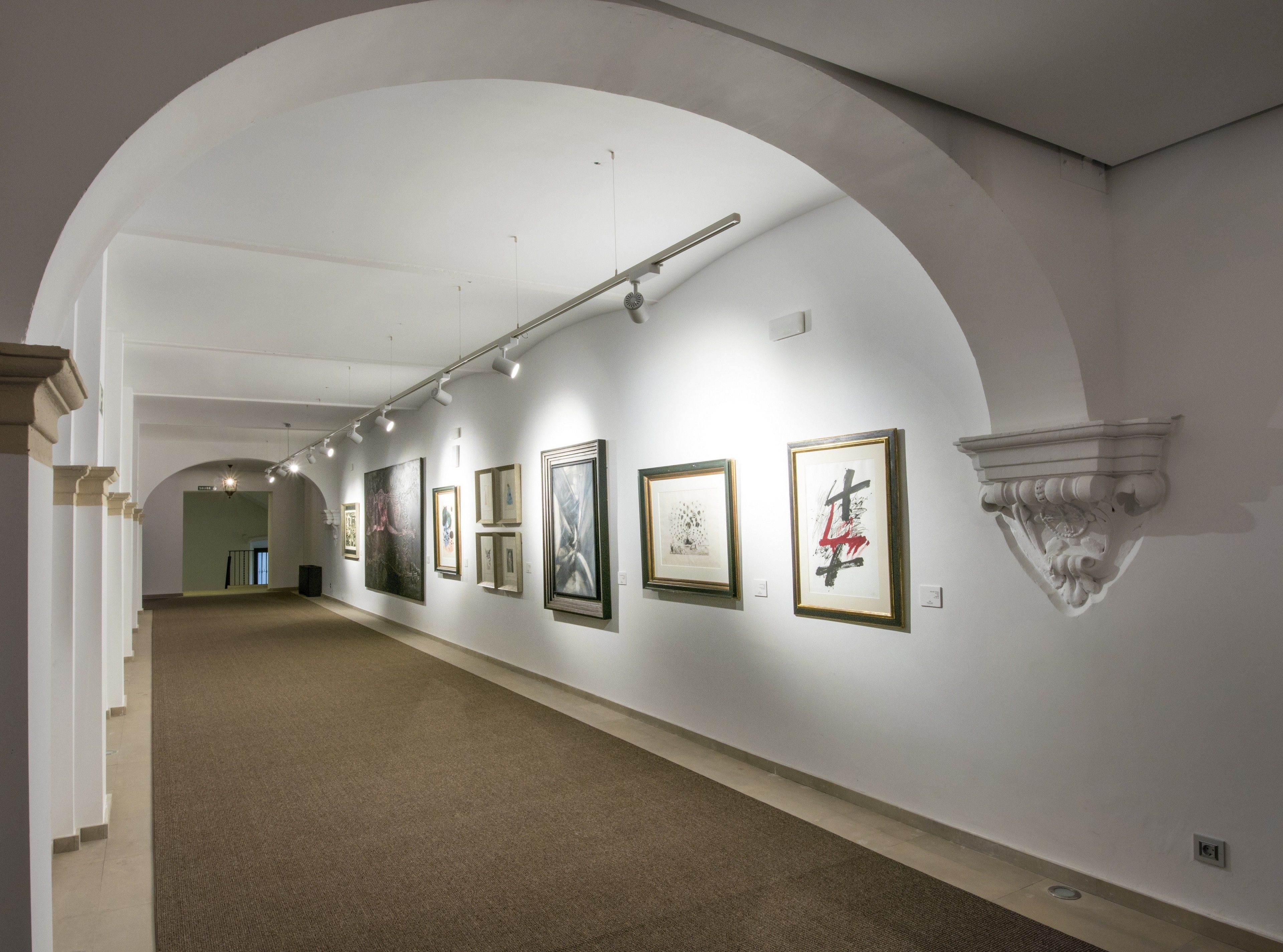 An art gallery with a long corridor lined with framed artworks on white walls.
