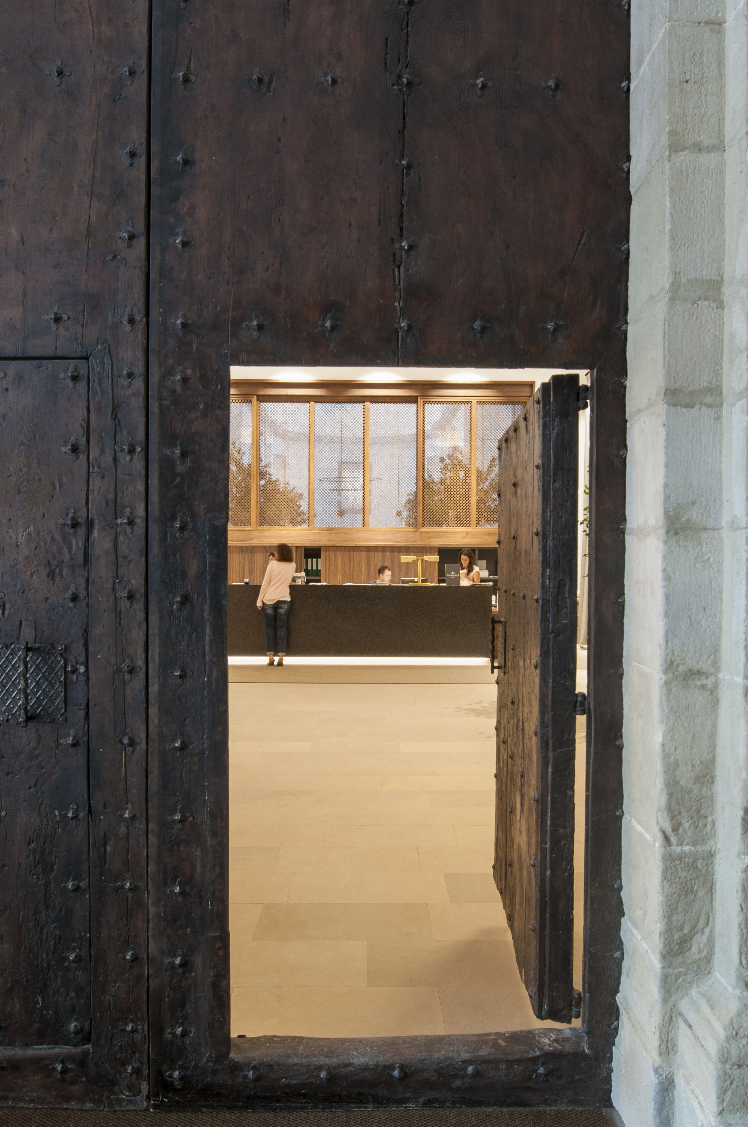 Une grande porte en bois, renforcée de clous en métal, qui donne sur un espace d’accueil comprenant un comptoir et une fenêtre.