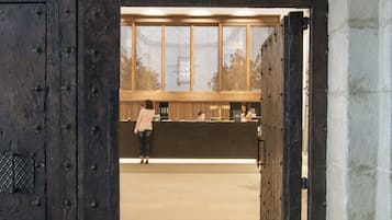 Une grande porte en bois, renforcée de clous en métal, qui donne sur un espace d’accueil comprenant un comptoir et une fenêtre.