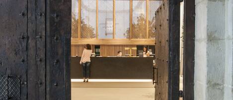 A large wooden door with metal studs, leading to a reception area with a counter and a window.