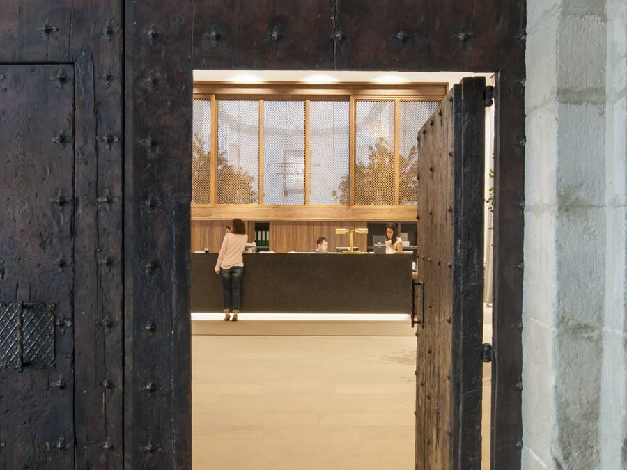 Une grande porte en bois, renforcée de clous en métal, qui donne sur un espace d’accueil comprenant un comptoir et une fenêtre.