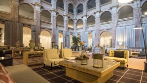 A spacious lobby with a high ceiling, featuring a central coffee table, seating area with sofas and armchairs, and a decorative plant centerpiece. - Parador de Lleida (Lleida)