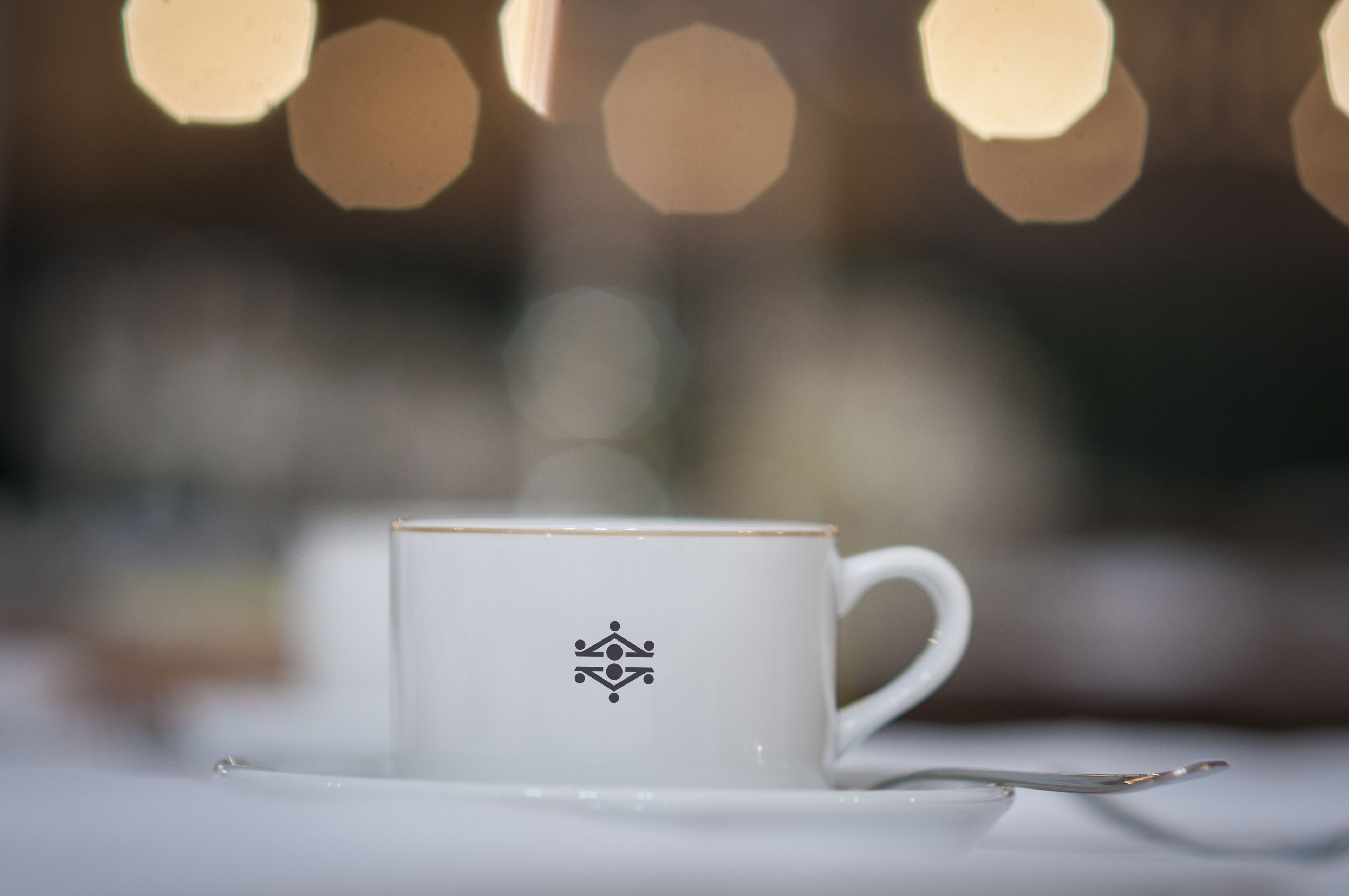 Eine weiße Tasse mit einem Logo auf einem Untertasse, auf einem Tisch platziert.