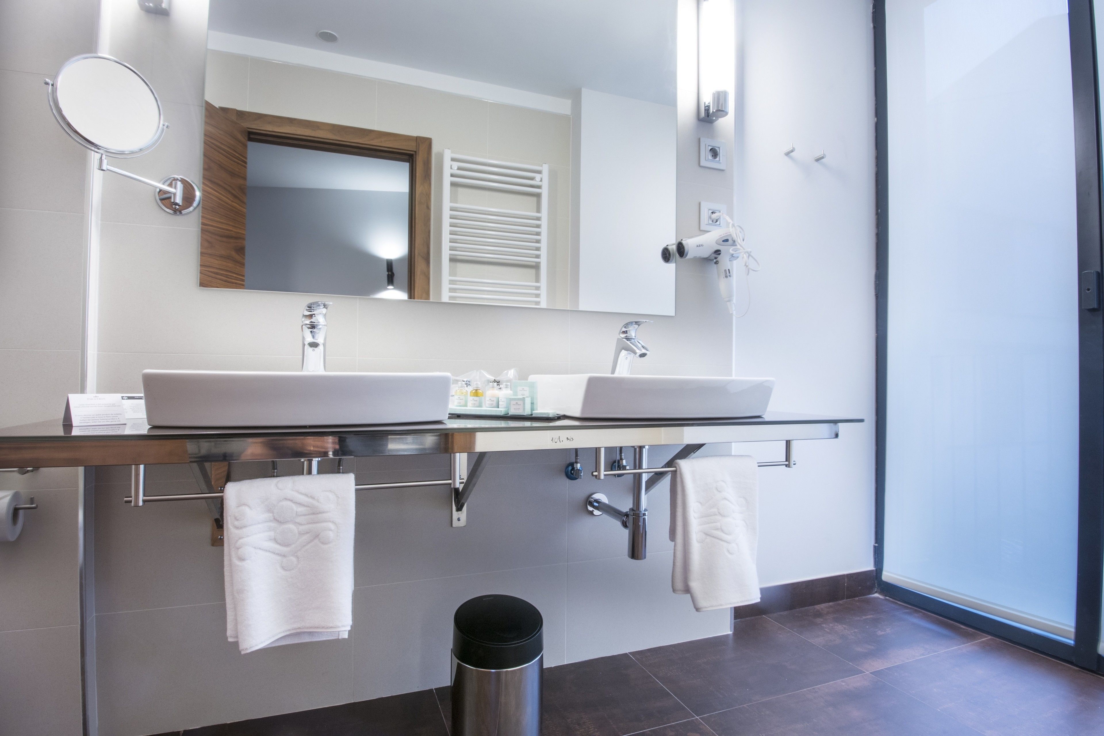 A modern bathroom with a dual sink vanity, towel racks, a mirror, and a hairdryer.
