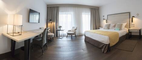 Una habitación de hotel con cama, escritorio, silla y una mesita de noche con lámpara.