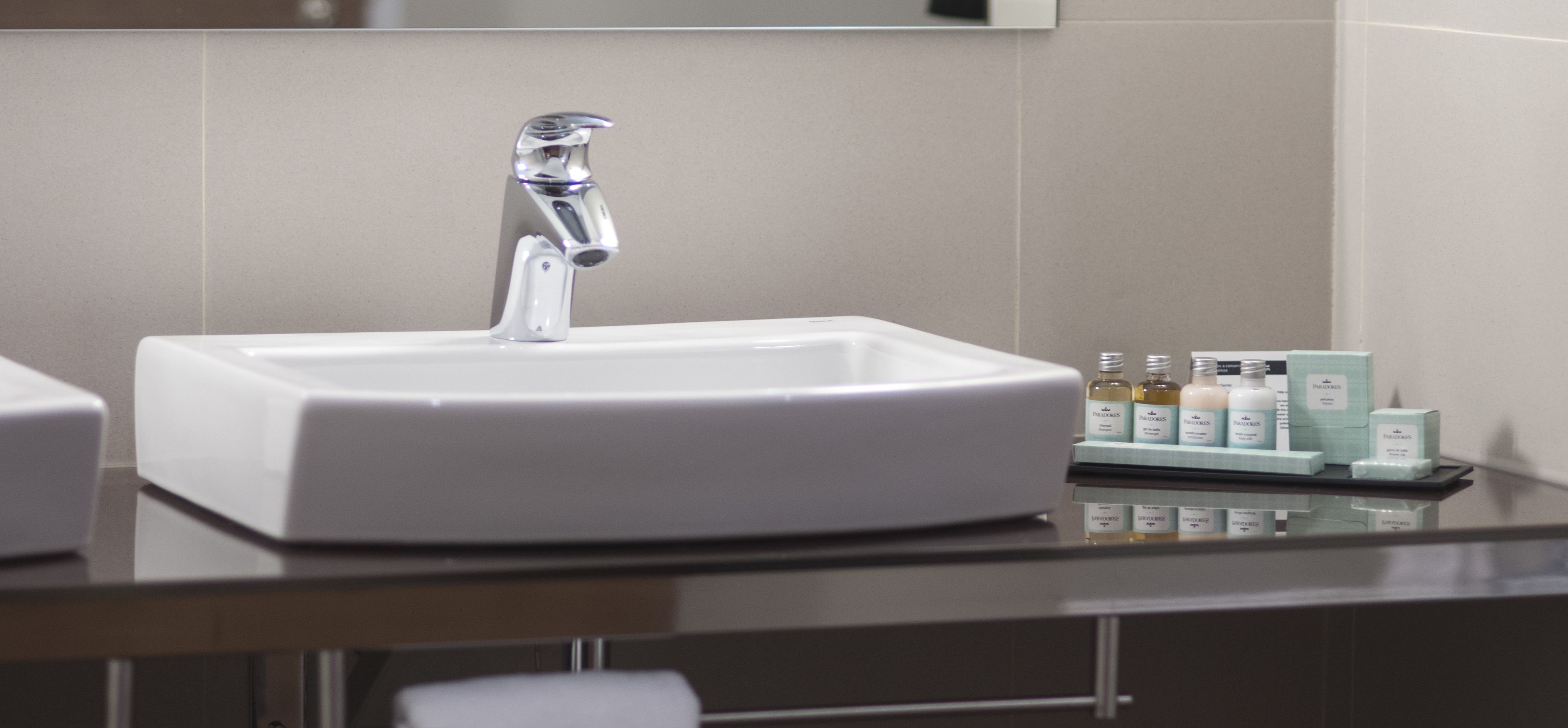 A modern bathroom with a white sink, a chrome faucet, and a small tray with toiletries.