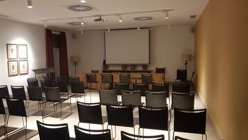 A conference room with a large screen, multiple rows of chairs, and ceiling lights.