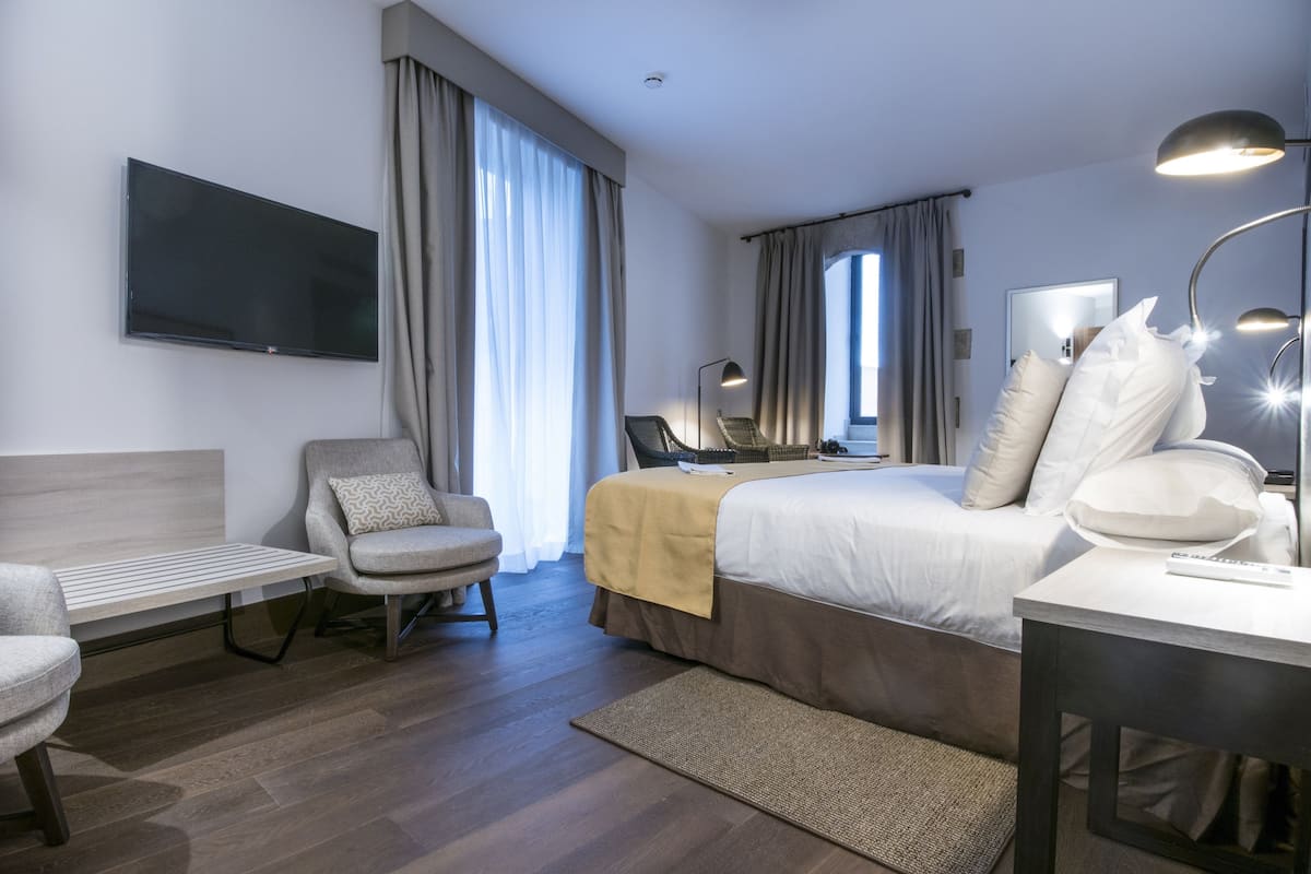 Una habitación de hotel moderna con una cama, un escritorio, una silla, un televisor y una lámpara.
