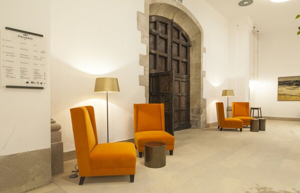 A hotel lobby with a wooden door, orange chairs, and a reception desk.