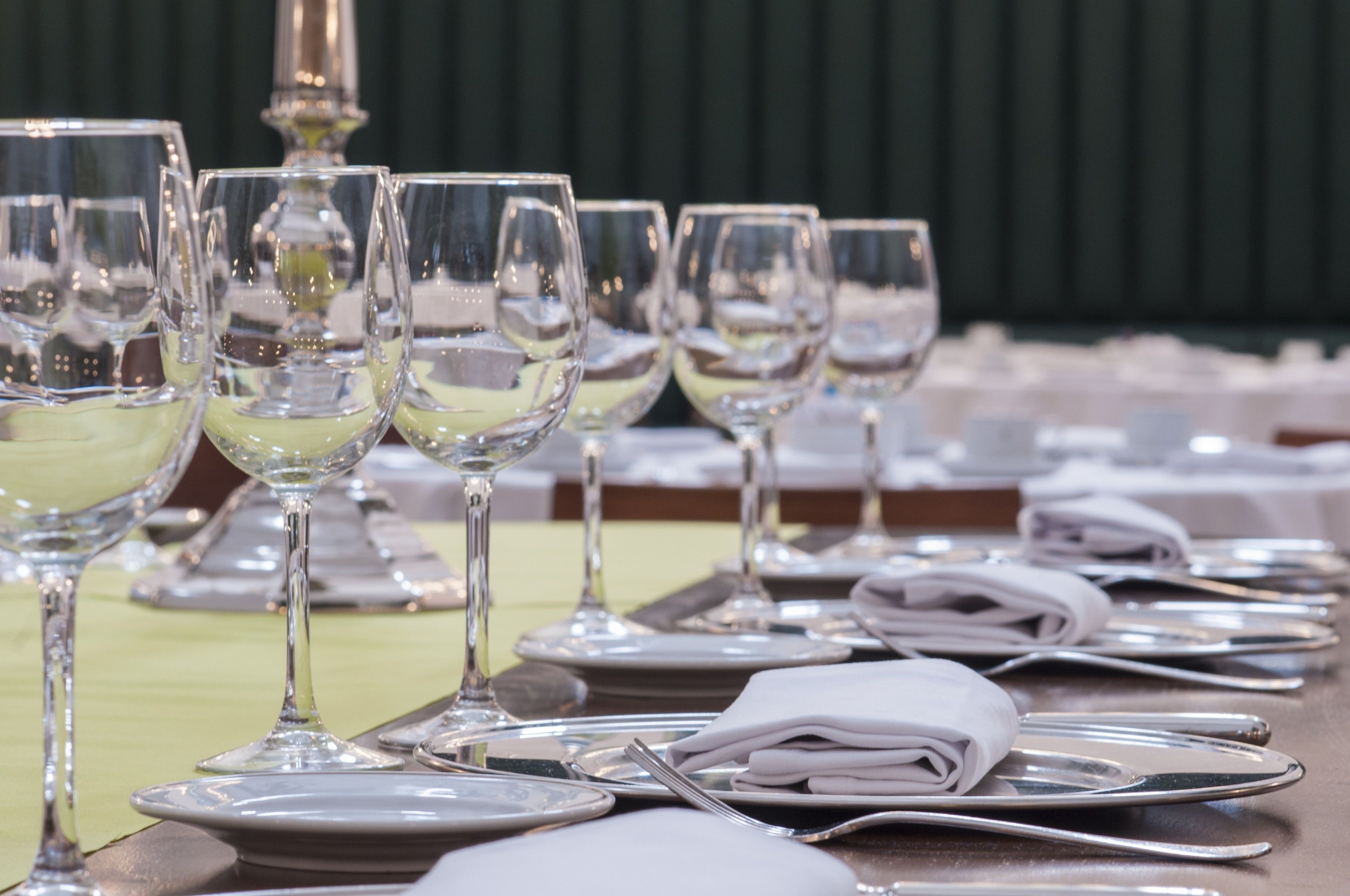 Mesa posta com vários copos de vinho, pratos e guardanapos dobrados, indicando uma disposição formal para refeição.