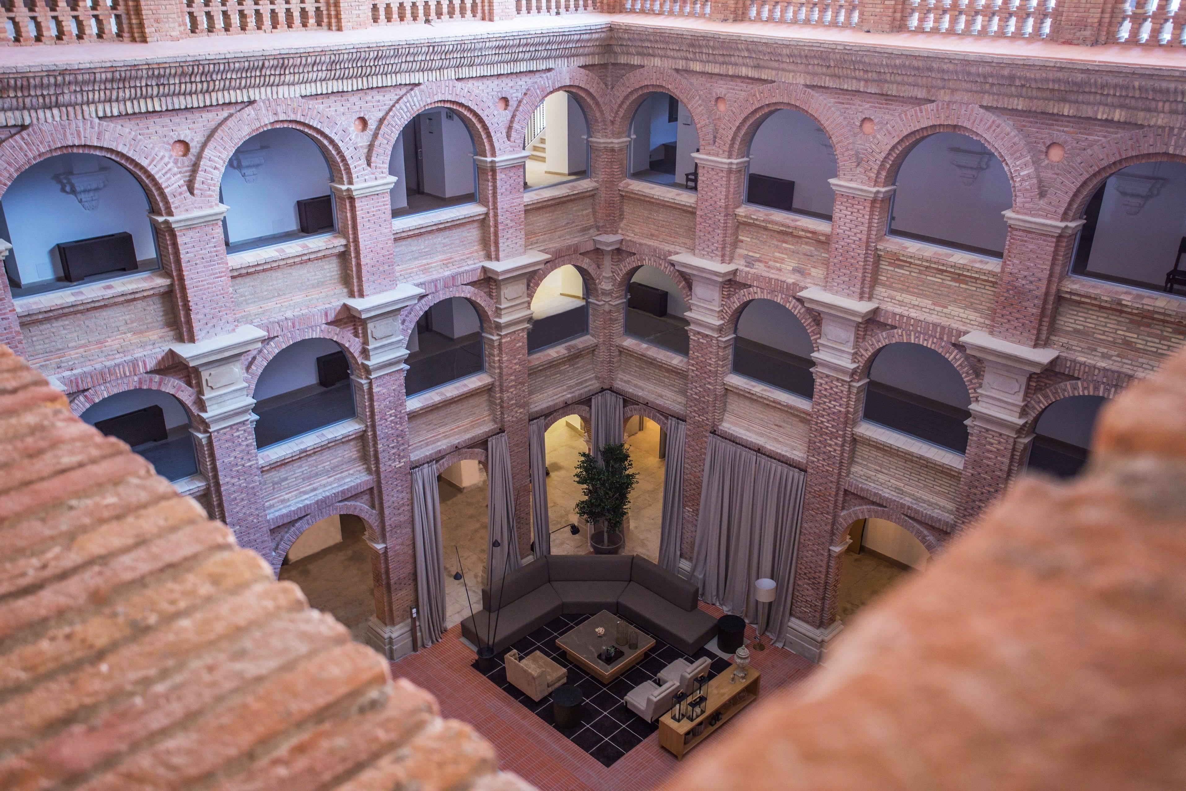 Un atrio de varios niveles con arquitectura de ladrillo, múltiples arcos y una zona de estar central con una mesa de café y sofás.