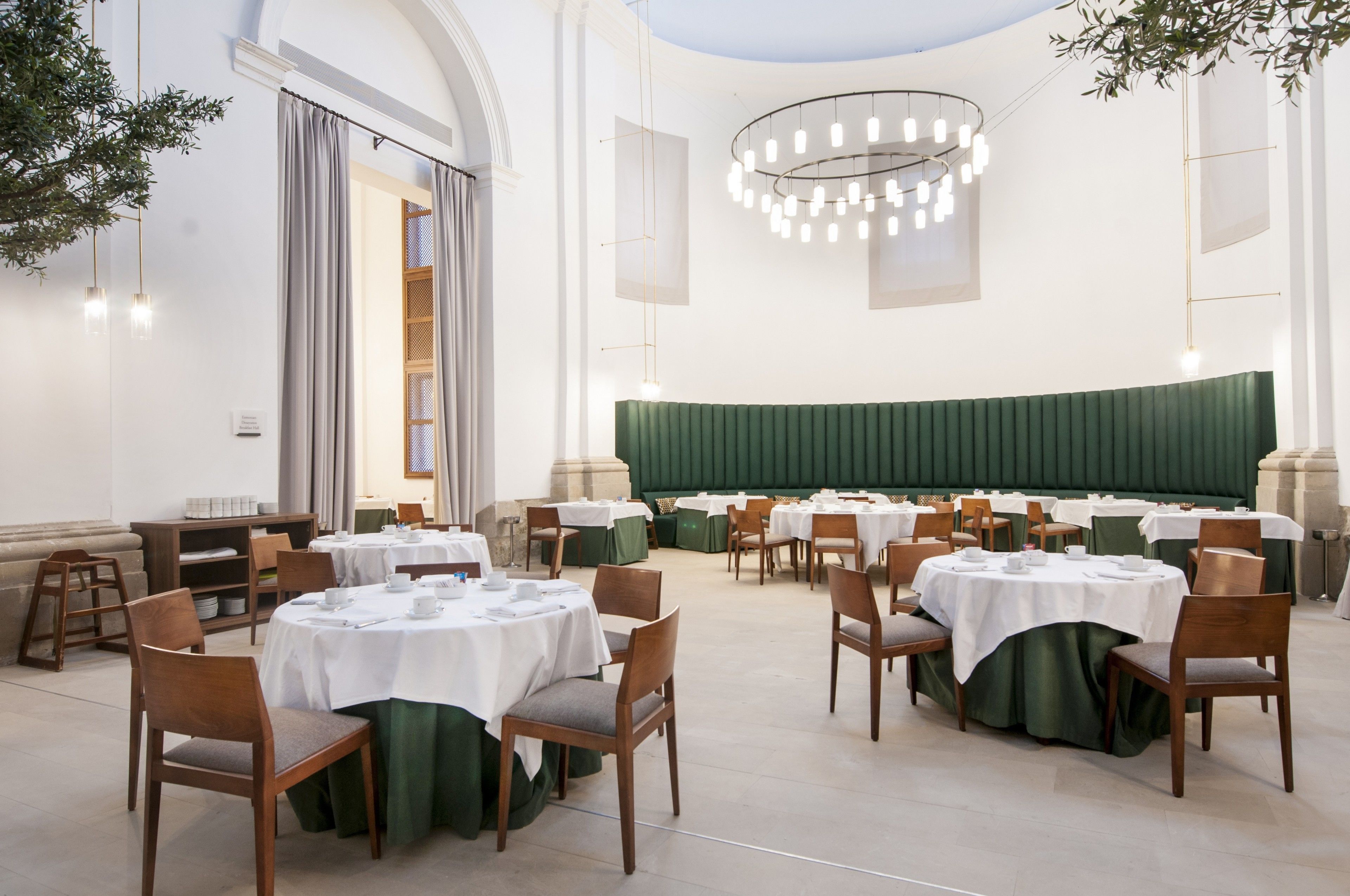 A formal dining room with round tables, chairs, and a green upholstered wall.