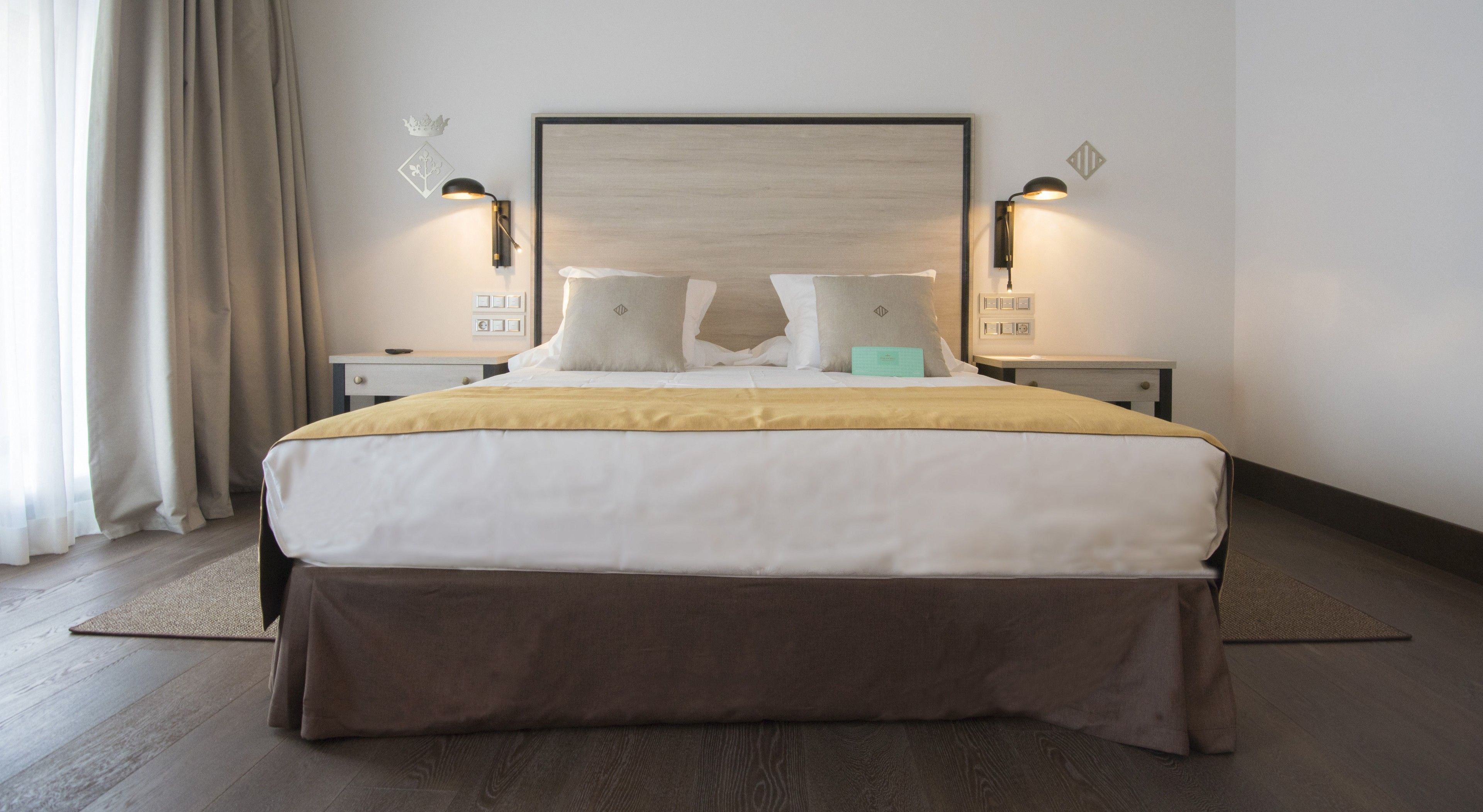Habitación de hotel con una cama grande, dos mesitas de noche, un tablero de noche, cabecero y lámparas fijadas a la pared.