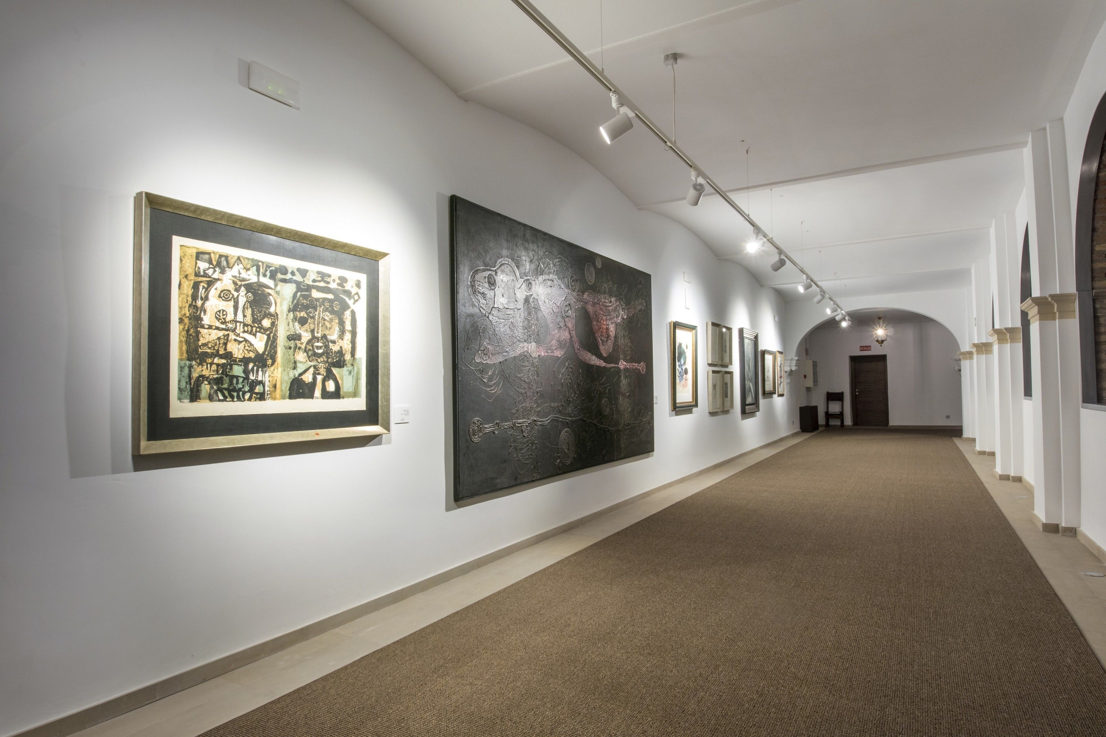 An art gallery with framed artworks on white walls and a carpeted floor.