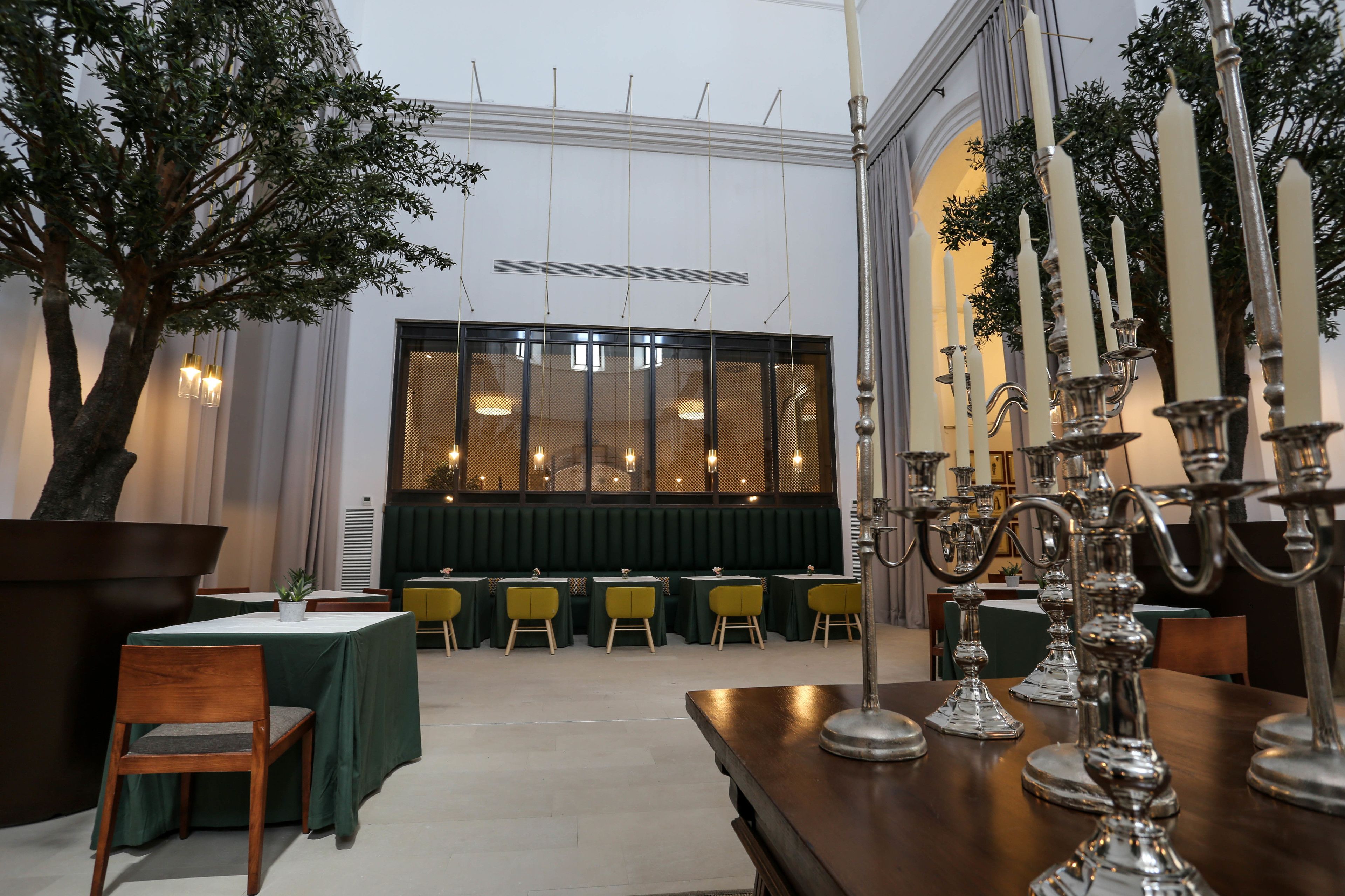 Un comedor con mesas y sillas, un árbol grande y un candelabro decorativo.
