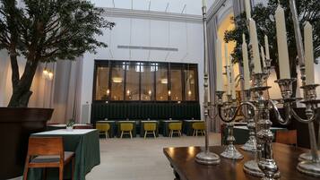 Un comedor con mesas y sillas, un árbol grande y un candelabro decorativo.