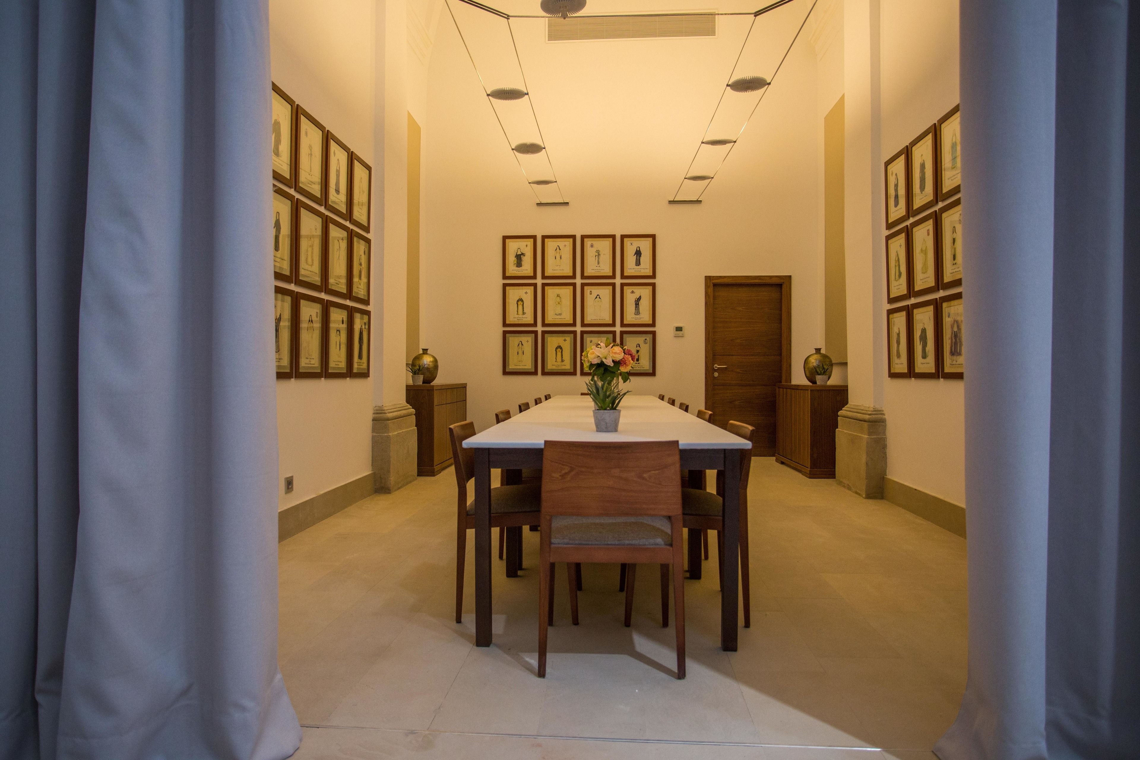 Un comedor con una mesa larga, varias sillas, cuadros en las paredes y una planta en maceta sobre la mesa.
