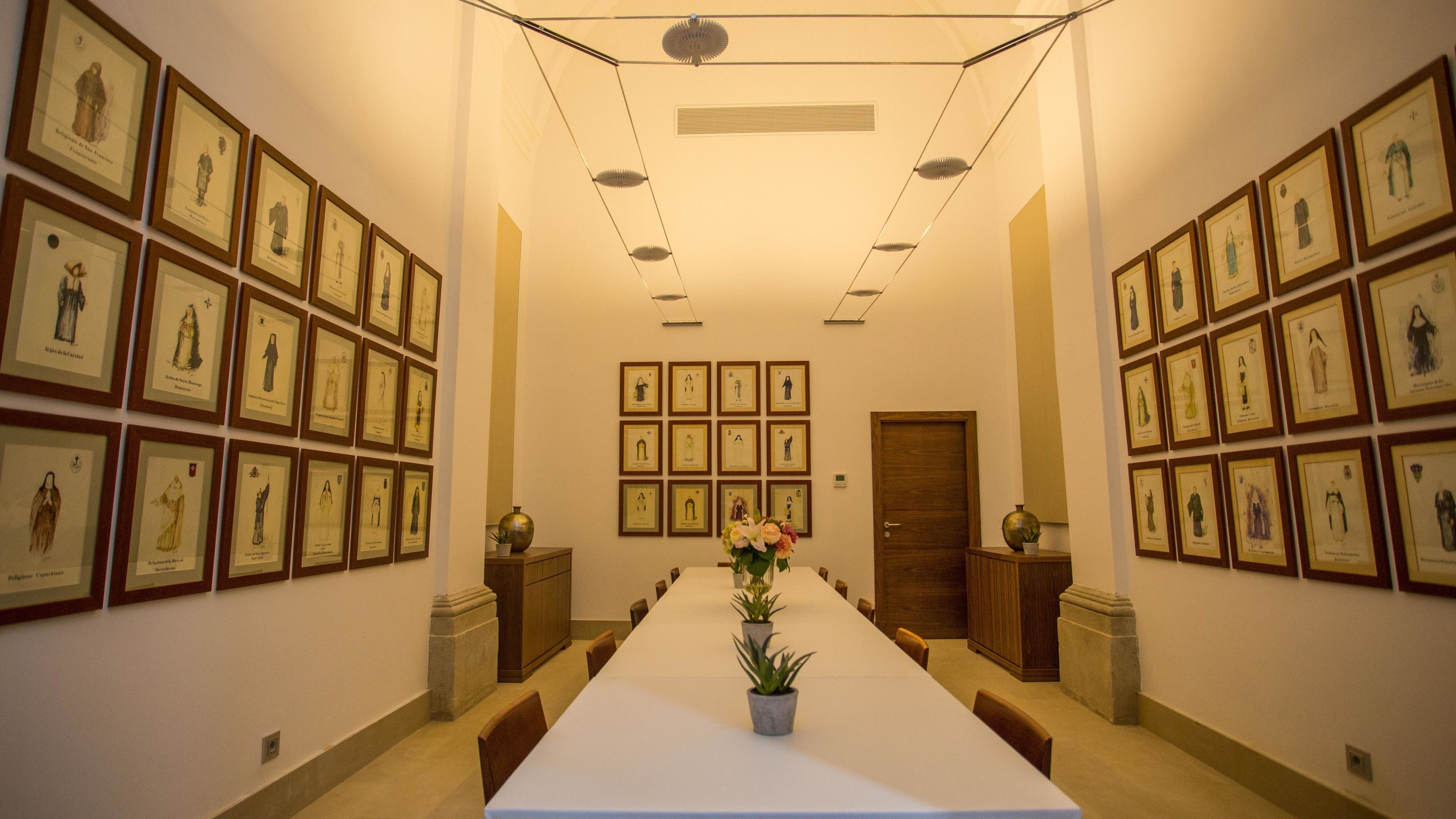 Une salle de conférence avec une longue table, des œuvres d’art encadrées accrochées aux murs et une porte au fond de la pièce.