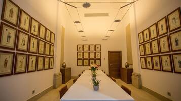 Une salle de conférence avec une longue table, des œuvres d’art encadrées accrochées aux murs et une porte au fond de la pièce.