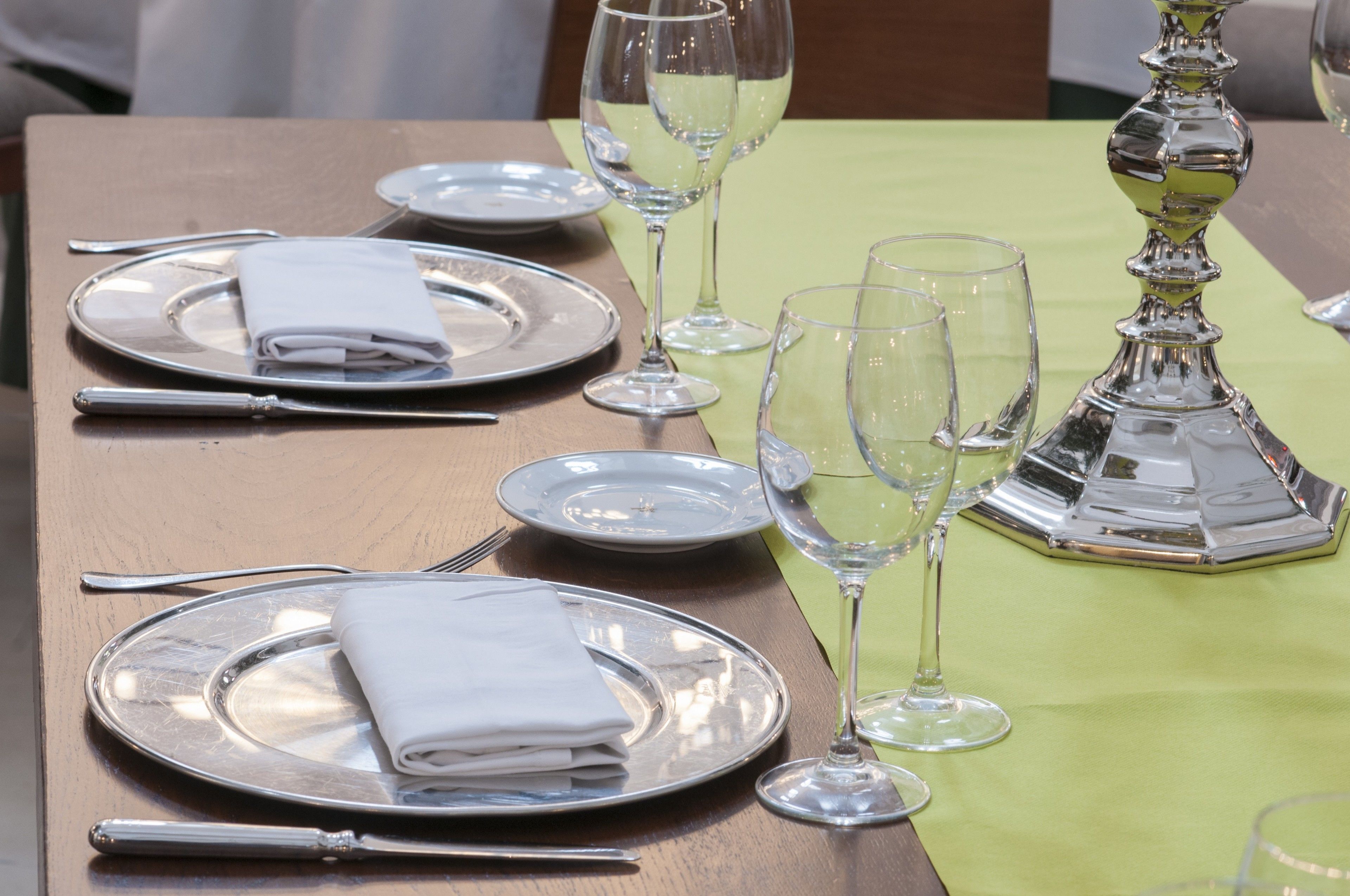 A table set with silverware, plates, and wine glasses, with a green tablecloth and a silver candelabra.
