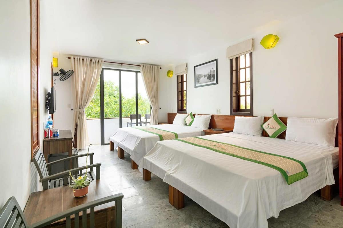 A hotel room with two beds, a dining table, chairs, a small desk, and a potted plant.