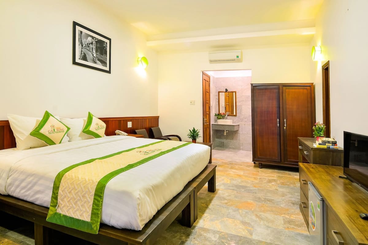 A hotel room with a bed, a desk with a TV, a wardrobe, and a bathroom visible through an open door.
