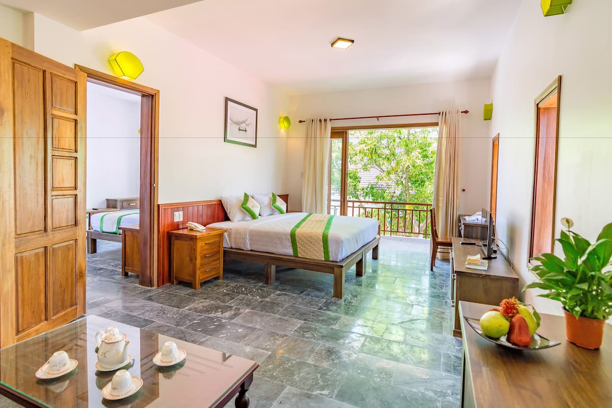 A hotel room with a bed, bedside table, and a balcony with a view of greenery.
