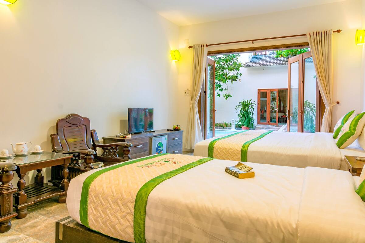 A hotel room with two beds, a desk with a chair, a television, and a view of the outside.