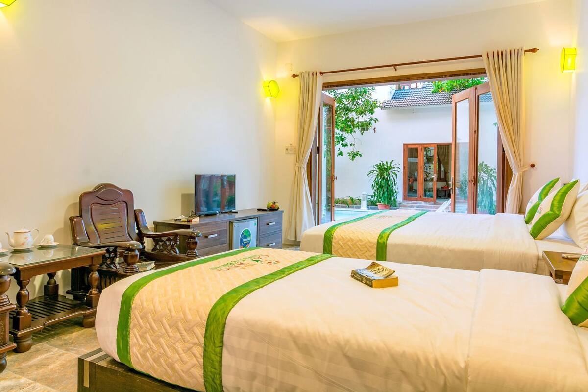 A hotel room with two beds, a TV, a desk with a computer, and a view of a pool and outdoor area.