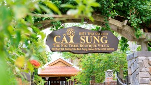 A sign for "Cây Sung The Fig Tree Boutique Villa" with a stone archway and a brick wall in the background. - Fig Tree Boutique Villa (Da Nang)