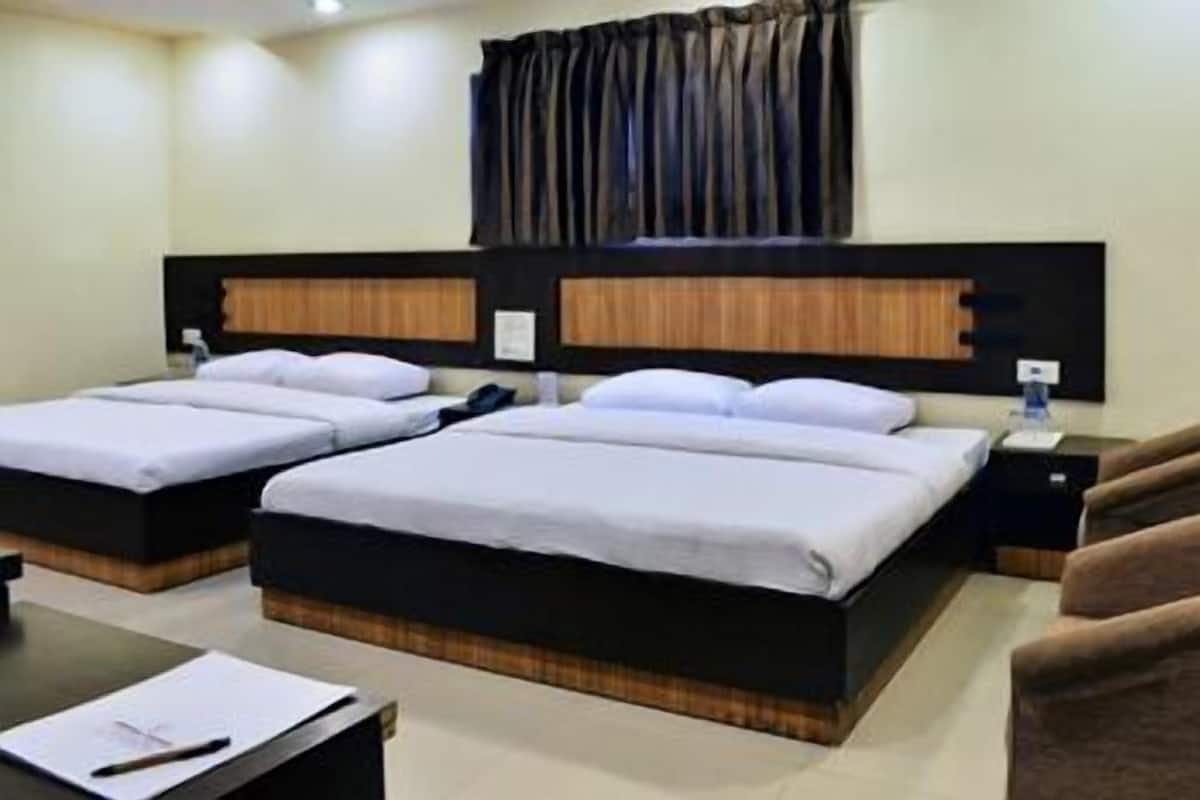 A hotel room with two beds, wooden headboards, a desk with a chair, and a nightstand with a lamp.