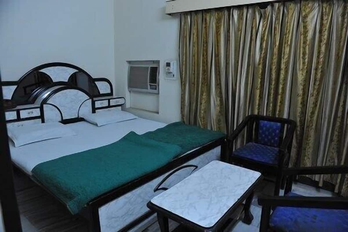 A hotel room with a bed, a chair, a small table, and a window with curtains.