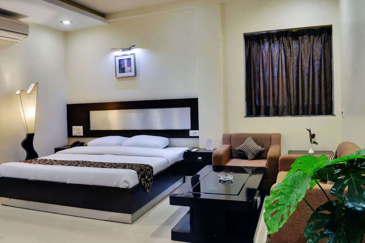 A modern hotel room with a large bed, a sofa, a coffee table, and a potted plant.