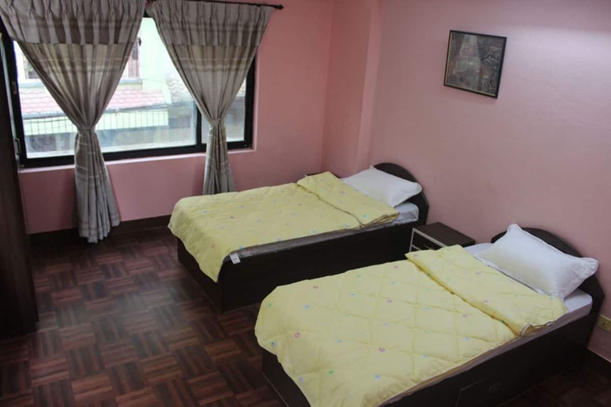 A room with two beds, each with a yellow quilt, a window with curtains, and a picture on the wall.