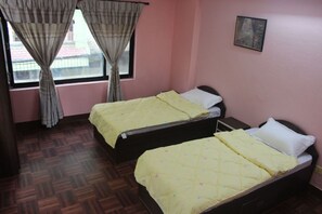 Une chambre avec deux lits, chacun recouvert d’une courtepointe jaune, une fenêtre avec des rideaux et un tableau accroché au mur.