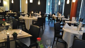 Un restaurant avec de nombreuses tables dressées pour le dîner, chacune étant recouverte d’une nappe blanche, agrémentée de verres à vin et de bougies.