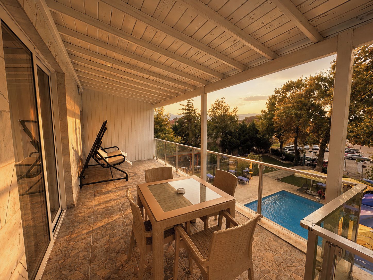 Un espacio al aire libre cubierto con una piscina, una mesa con sillas y un vidrio que da a la zona de la piscina.