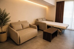 Ein modernes, kompaktes Wohnzimmer mit einer Couch, einem kleinen Tisch und einem Bett mit Matratze.