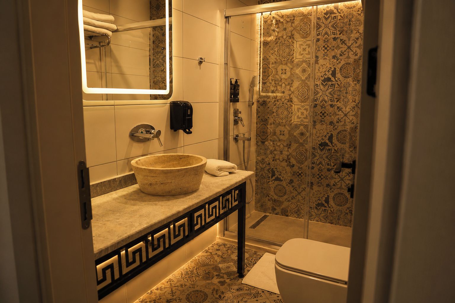 Un baño con lavamanos de piedra, una toalla, un inodoro y una ducha con azulejos estampados.