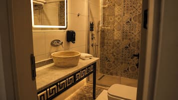 Un baño con lavamanos de piedra, una toalla, un inodoro y una ducha con azulejos estampados.