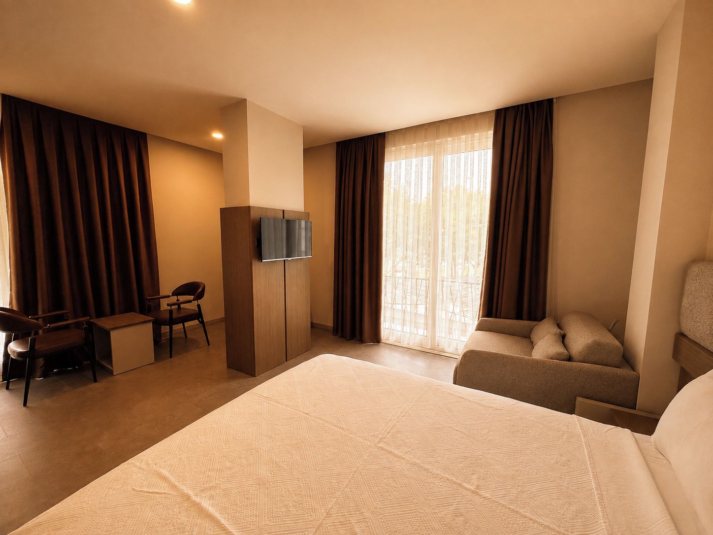 A hotel room with a large bed, a desk with a chair, a television, and a sofa.