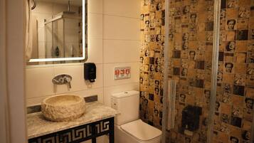 A bathroom with a stone sink, a mirror, a toilet, and a shower.