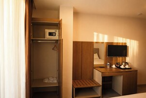 Habitación de hotel con escritorio de madera, televisor, espejo, armario y un pequeño banco.