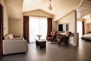 Una habitación de hotel moderna con sofá, sillones, televisor de pantalla plana y cama.